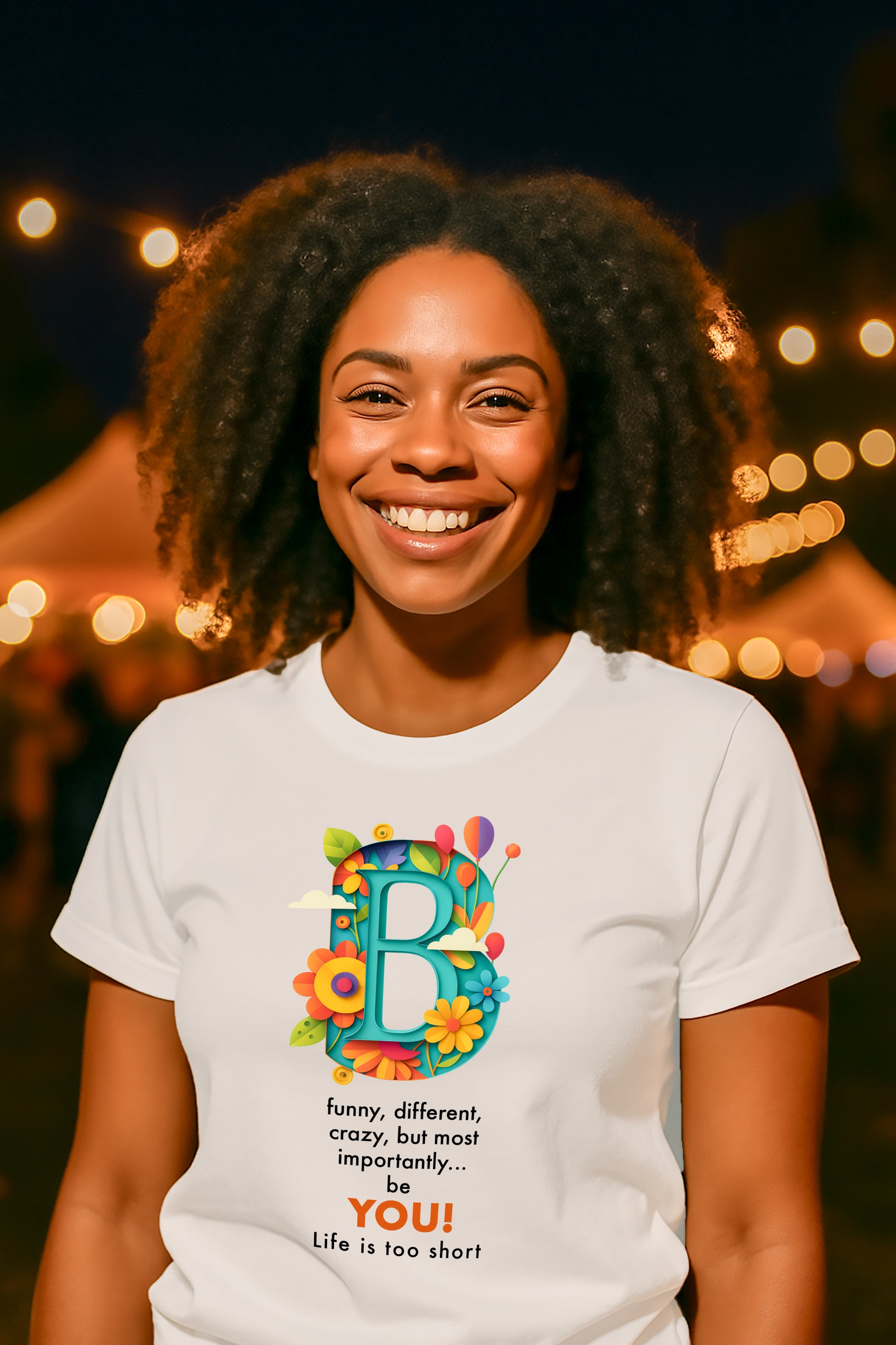 Person wearing a white t-shirt with a colorful "B" design and text, standing with lights in the background.
